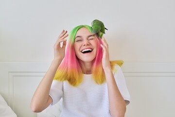 Trendy fashionable with colored hairstyle teenager with green parrot on head