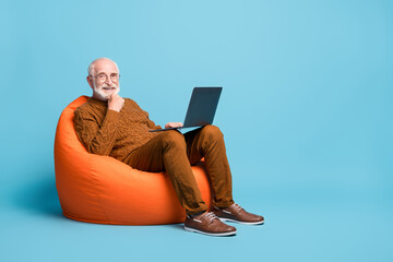 Portrait of his he nice attractive cheerful skilled smart clever bearded grey-haired man sitting in bag chair using laptop calling video isolated over blue pastel color background