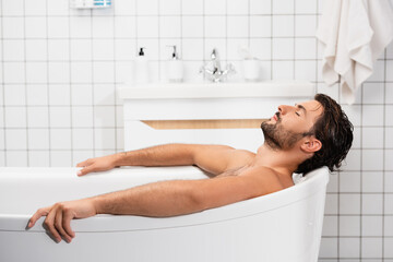 Bearded man taking bath with closed eyes at home