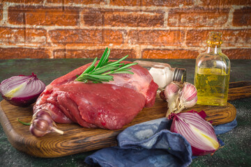 Wall Mural - Raw meat, beef fillet, large piece on a cutting board with spices for cooking. Black dark green background, copy space