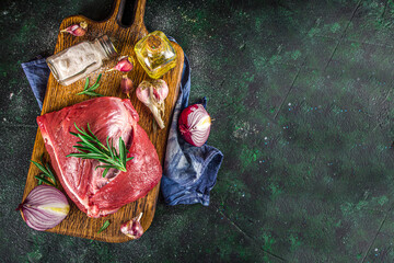 Wall Mural - Raw meat, beef fillet, large piece on a cutting board with spices for cooking. Black dark green background, copy space