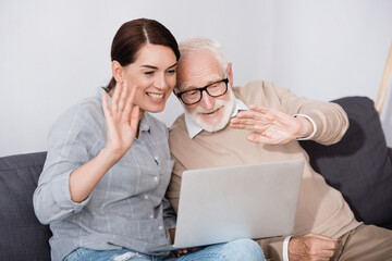 Wall Mural - cheerful elderly man with daughter waving hands while having video chat on laptop