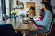 © Inti St. Clair - Dad feeding baby while working from home on laptop computer at dining room table
