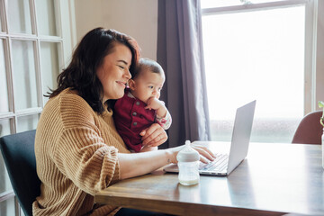 Mother doing video chat with baby on laptop computer at dining room table 