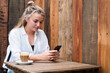 © Mint Images - Young blond woman sitting alone at an outdoor cafe table, checking her mobile phone.