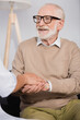 © LIGHTFIELD STUDIOS - smiling senior man holding hands with social nurse at home on blurred foreground