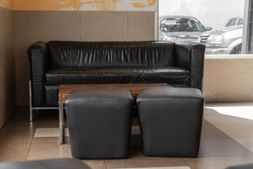 interior decoration, room with a sofa and 2 black leather puffs in the middle of a table, next to a window, modern furniture