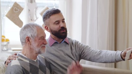 Poster - Mature man and senior father with smartphone indoors at home at Christmas, video call concept.