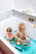 © Melissa Milis Photography/Stocksy - Sensory Bath Time Play for a baby girl and toddler boy with colorful pompons and blue water