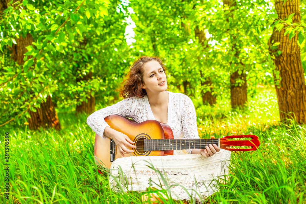 Woman playing acoustic guitar in central park Cute young adult girl sit ...