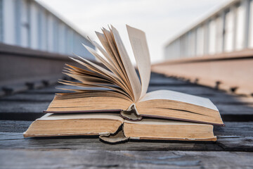 Two old retro vintage aged used book lie on wooden sleepers of railway between metal fence of grunge style bridge on blue sky  background Education development symbol sign concept