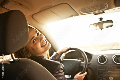 Cuadros en Lienzo woman in car indoor keeps wheel turning around smiling looking at passengers in