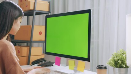 Wall Mural - Startup small business, Young Asian woman checking online order on computer with green screen. and packing boxes for products to send to customers.