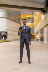 Wall Mural - Full length shot of African businessman standing outdoors using phone