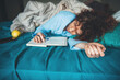 Caucasian woman lying sleepy in bed is reading something from a book wearing blue pajama late night