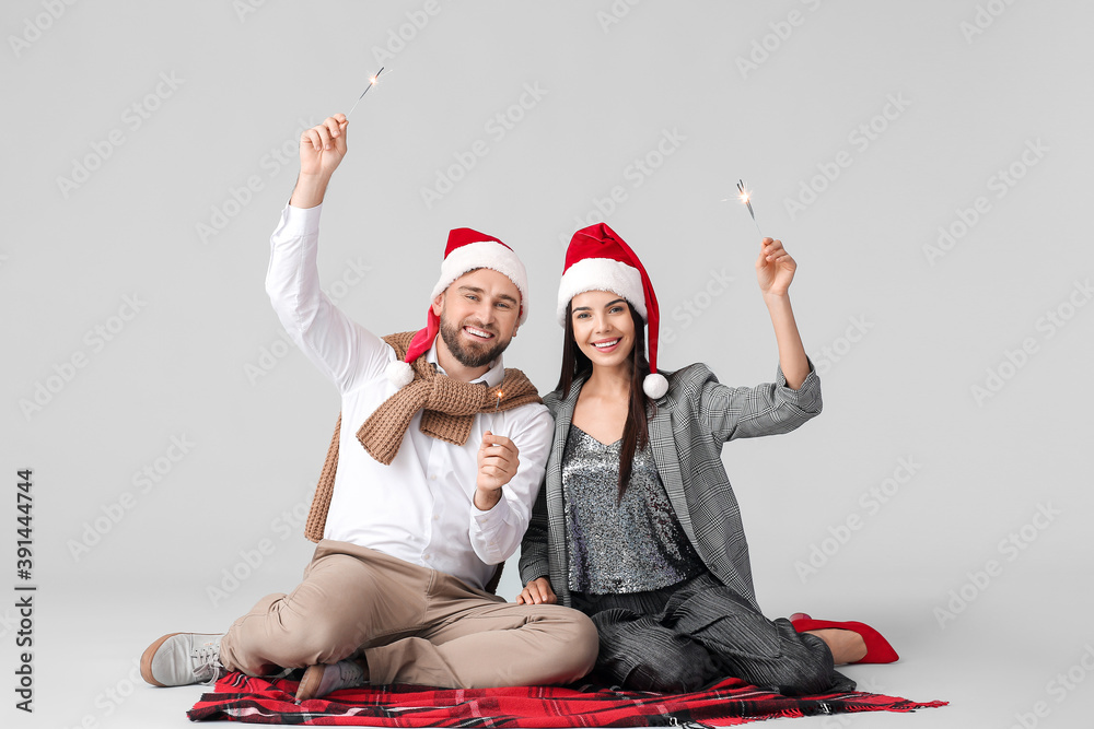 Young couple with Christmas sparklers on grey background