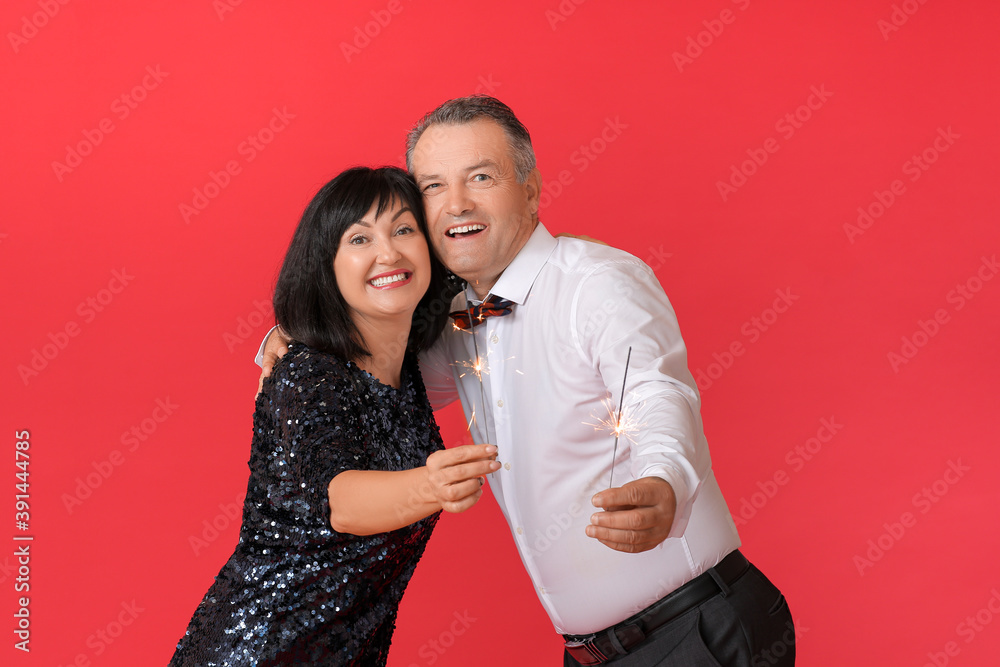 Mature couple with Christmas sparklers on color background