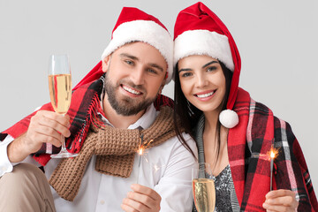 Poster - Young couple with Christmas sparklers and champagne on grey background