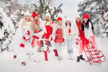 A large group of girls with Christmas gifts in their hands standing in the winter forest.Girls in red and white clothes with Christmas gifts in the snowy forest