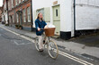 © Mint Images - Young blond woman cycling down a village street.