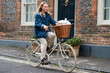 © Mint Images - Young blond woman cycling down a village street.