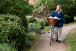 © Mint Images - Young blond woman pushing bicycle with basket along footpath.