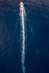 Wall Mural - aerial view of a boat sailing over blue water and leaving a trail of white bubbles