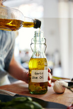 Woman Pouring Olive Oil Into Bottle Containing Garlic