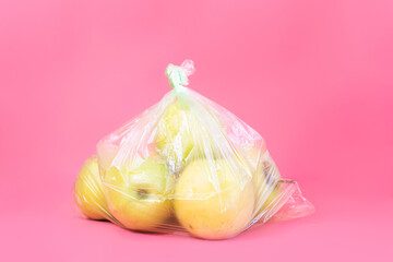 Wall Mural - Fresh yellow-green apples in a plastic bag on a pink background.