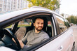 © dikushin - Happy bearded young man sitting in car and using cell phone, side view, looking away. Handsome businessman using mobile phone in auto. M