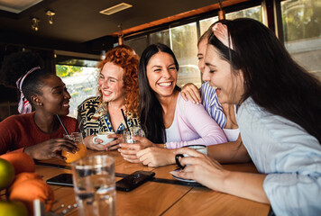 Group of young female friends having fun in coffee shop, talking and laughing while sitting at table.