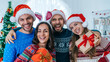 © wpadington - Group of young people posing in Santa hats and knitted sweaters with gift boxes in hands smiling to the camera