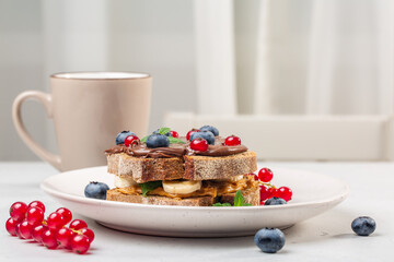 Breakfast table - multigrain bread with organic peanut butter and chocolate  butter, and berries, cup with hot drink. 