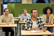 © Friends Stock - Young cheerful mixed race male office worker sitting listening to coach during seminar or training and smiling while studying with colleagues in coworking space