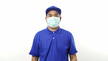 Wall Mural - Asian delivery man in blue uniform wearing protection mask and medical rubber gloves standing on isolated white background. 4k Resolution.