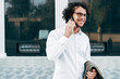 © iuricazac - A successful businessman with curly hair smiling while talking with his colleague on a mobile phone. A happy curly male wearing a white shirt has a joyful expression during speaking on a cellphone.