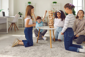 Group of happy kids playing wood block tower stacking game at home or in after school leisure club