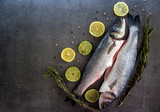 Fototapeta Tęcza - Fresh trout fish on a table with lemons and rosemary. Dark grey textured background with copy space. Balanced diet concept. 