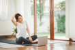 © interstid - Smiling Asian woman doing yoga neck stretching online class from laptop at home in living room. Self isolation and workout at home during COVID-19.
