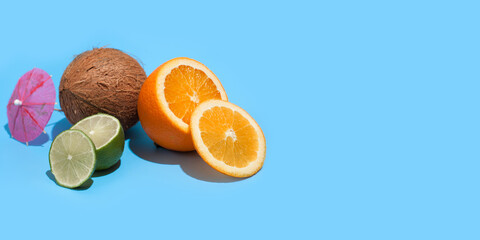 Wall Mural - Fresh juicy orange, coconut and green lime with a cocktail umbrella isolated on blue background. Concept of Healthy eating and dieting. Travel and holiday concept. Copy space. Free space for your text