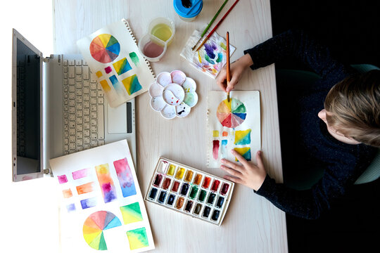Boy painting pictures with watercolor paints during art lesson. Pupil on drawing with brush. Watercolor color wheel and palette. Color theory beginner hobby lessons