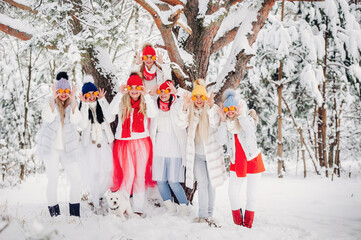 A large group of girls with tangerines are standing in the winter forest.Girls in red and white clothes with fruit in a snow-covered forest