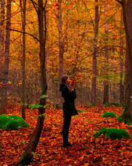 Autumn vibes. Young woman in autumn forest holding colorful maple leaves in hands. Romantic girl enjoy the fall season in woods with red carpet of leaves. Orange trees. Autumn outdoor lifestyle. 