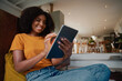 © StratfordProductions - Cheerful african woman sitting at home on floor with digital tablet at home relaxing
