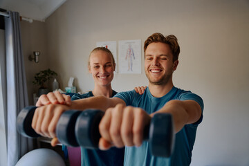 Smiling young female physiotherapist helping male patient do physical exercises to treat inflammation of the joints in arms