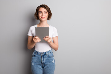 Wall Mural - Photo of cheerful young lady hold modern device tablet look empty space isolated over grey color background