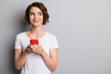 Poster - Photo of young attractive positive smile woman hold cellphone chat look empty space isolated over grey color background