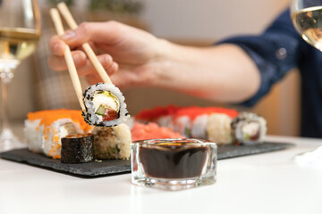 Womon holding sushi with sushi sticks on a white table with two glasses of wine