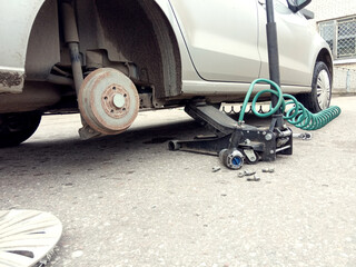 A car without a wheel, prepared for its replacement against the background of a Jack, side view - the concept of replacing seasonal tires