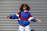 Fototapeta Boho - Cool black girl with curly hair, glasses, 90s, 80s, retro hip hop style, dancing against a metal wall, dynamics and expression